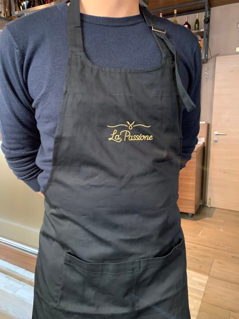 Schwarze Schürze mit goldener La Passione-Stickerei